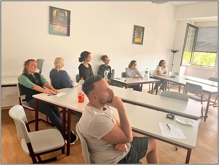 Teilnehmende sitzen in einem Schulungsraum an Tischen und verfolgen aufmerksam eine digitale Präsentation.