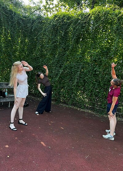 Drei Frauen machen gemeinsam Dehnübungen auf einem Sportplatz und neigen dabei den Oberkörper seitlich.