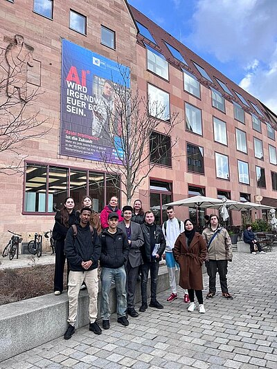 Ein Gruppenbild mit einigen jungen Erwachsenen und Jugendlichen vor einem Gebäude mit einer Banderole "Integrationsmesse 2026".