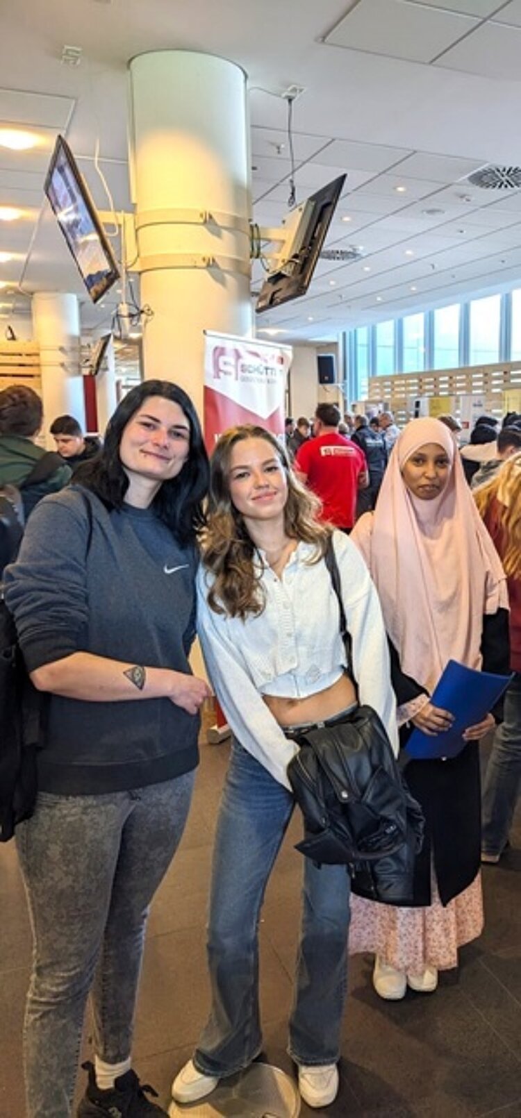 Drei Teilnehmerinnen der Werkstattschule des EBW Nürnberg stehen im Foyer des Fußballstadions und posieren gut gelaunt für ein Bild. 